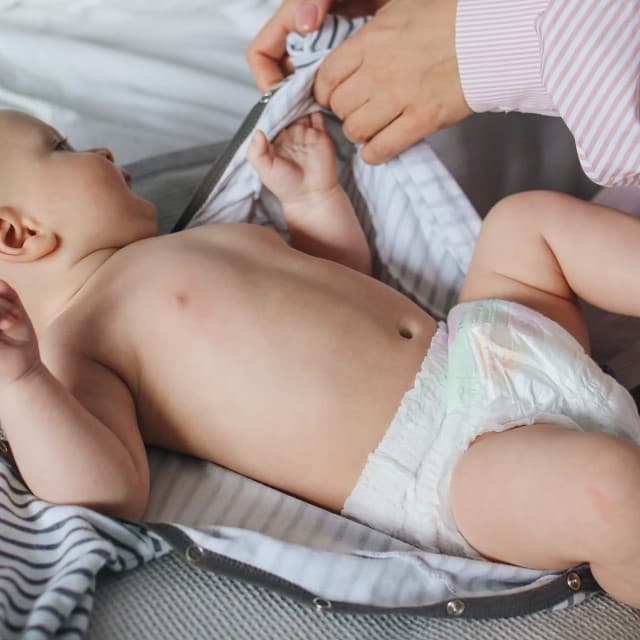 Et baby ligger på ryggen og er ved at få tøj på.