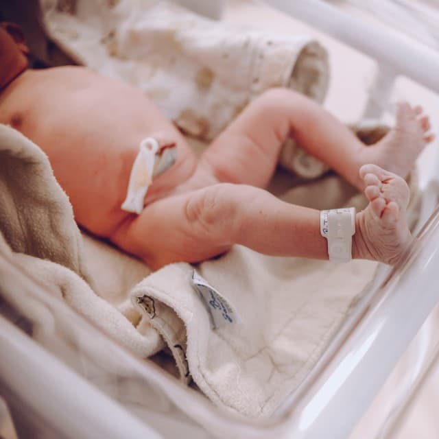 Nyfødt baby ligger i hospitalskrybbe med navleklemme på nyklippet navlestump.
