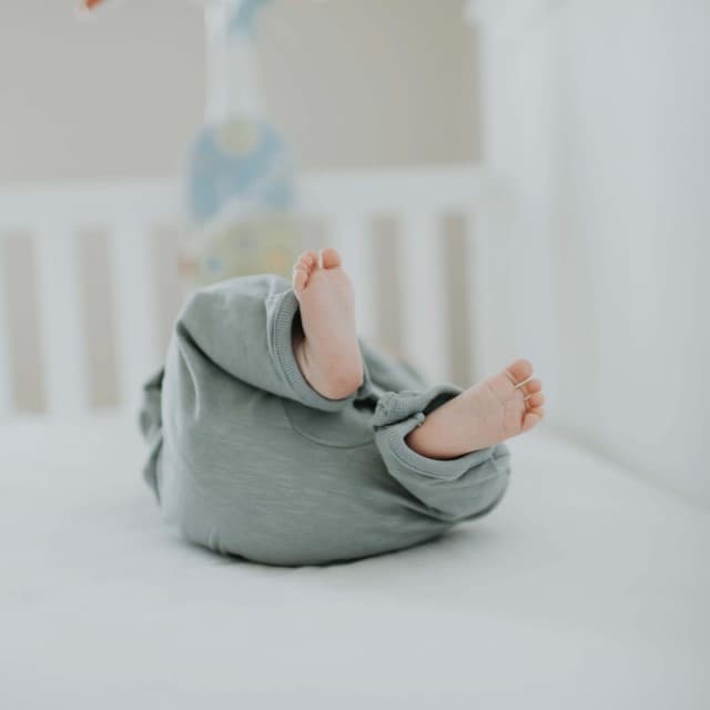 En baby ligger på ryggen i sovestilling.
