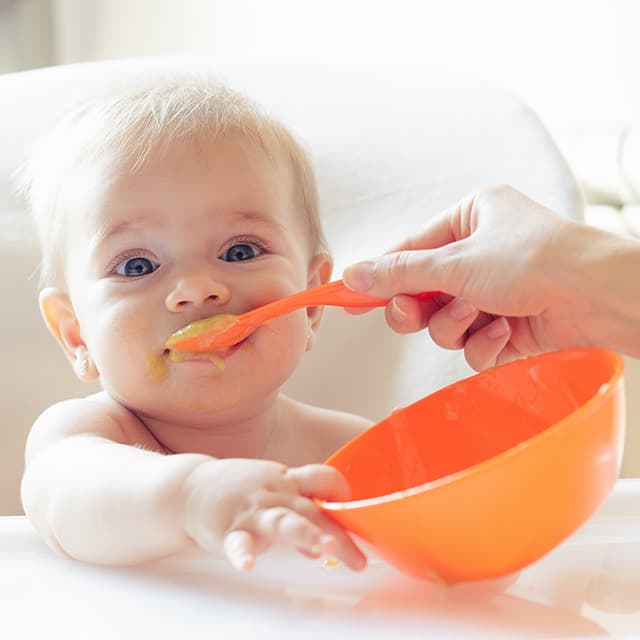 Glad baby bliver madet med babygrød.