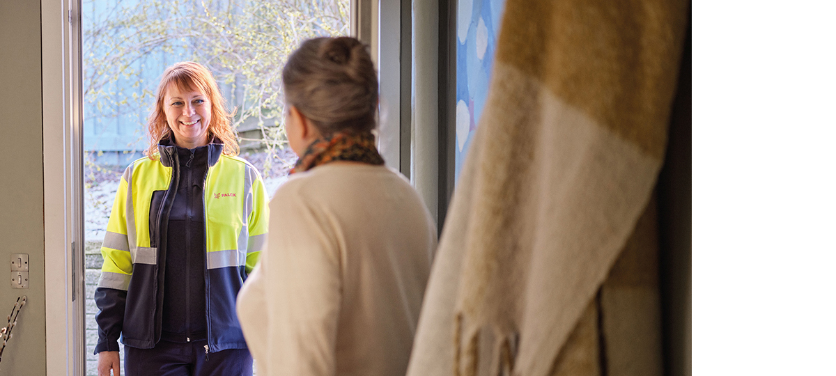 En falck medarbejder i gul refleksjakke står smilende i en åben dør og bliver mødt af en ældre kvinde indenfor i hjemmet.