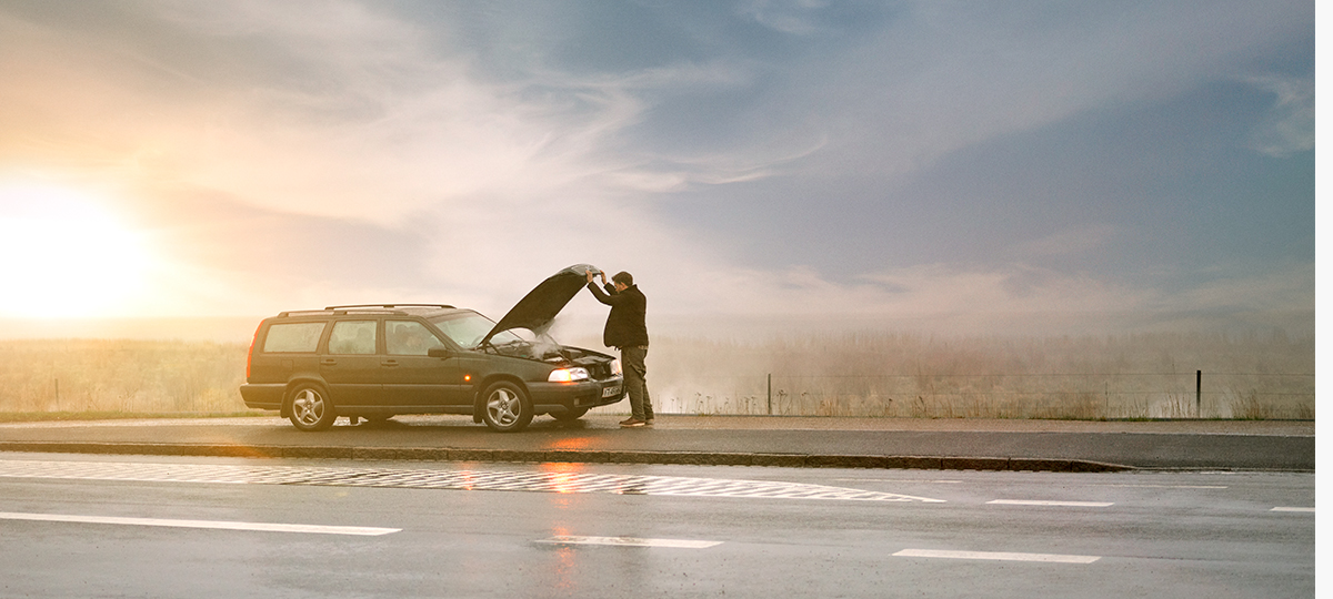 Mand står i vejkansten med sin bil og motorhjelmen slået op.