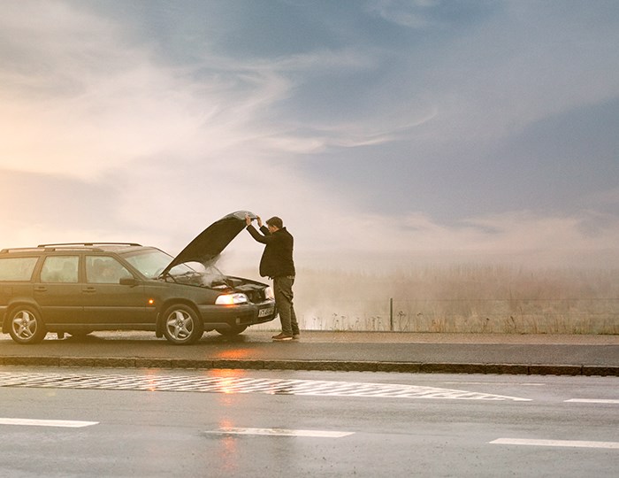 Mand står i vejkansten med sin bil og motorhjelmen slået op.