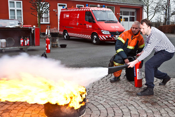 En mand vejledes af en Falck-redder i brandslukning