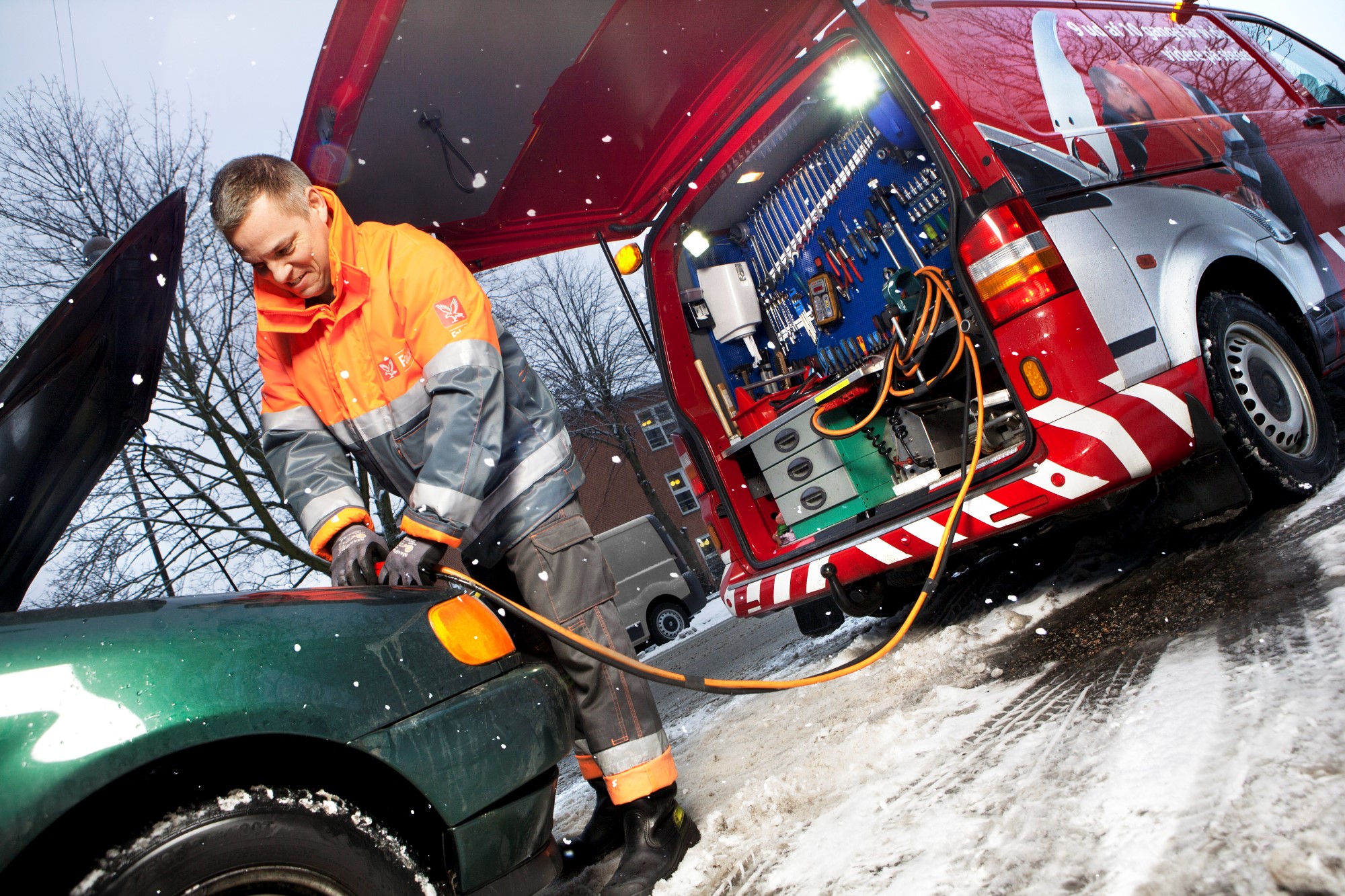 Vejhjælpsredder giver bil strøm i snevejr. 