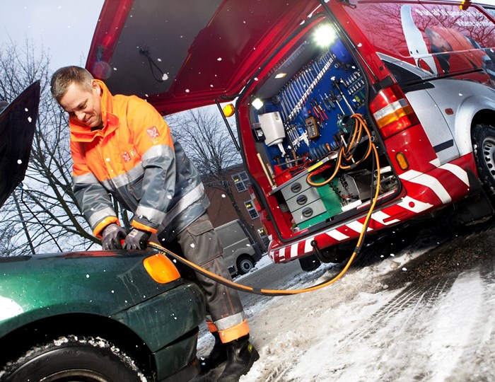 Vejhjælpsredder giver bil strøm i snevejr.